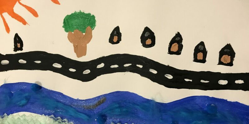 VIC - I am J. I live next to a big river that runs through the town. I like where I live because the sun sparkles onto the water. There is grass and moss that goes by the river. Where I live is really beautiful. You can see all the houses in my street. I feel safe where I live and I am very happy with my neighbourhood. There is a gap between the houses where I have drawn a tree. It is usually sunny where I live and sometimes there are clouds.